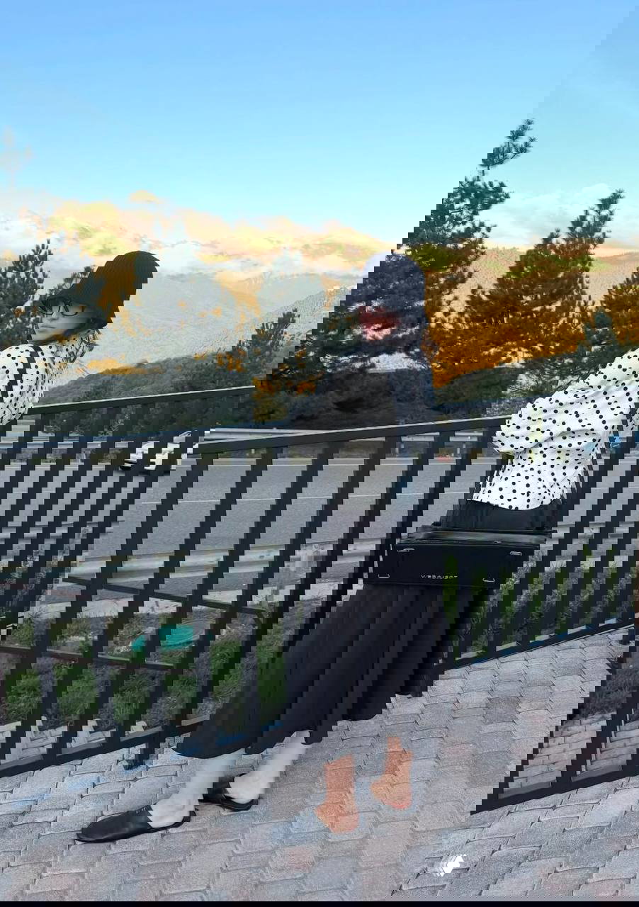 Лиза в белом гороховом жакете и черной юбке на смотровой площадке с горами позади — контрастный образ с ретро-нотами и шляпой клош.