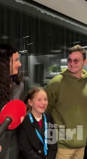 Трое людей улыбаются перед микрофоном в помещении: взрослая слева, ребёнок в центре и мужчина справа; логотип the girl.