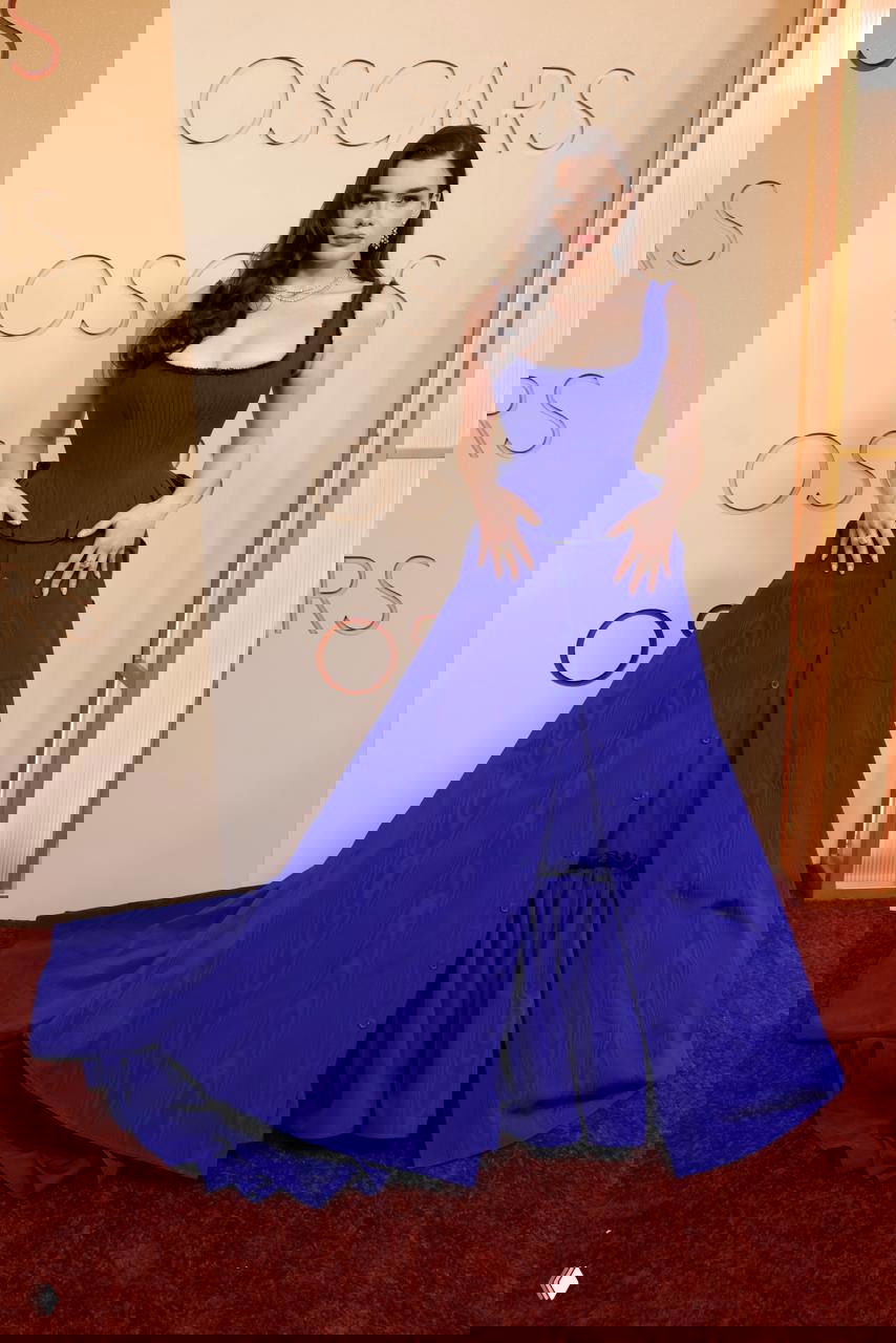 Полный рост женщины в длинном ярко-синем платье с корсетом и шлейфом на ковровой дорожке «Оскара», видно детали фасона и ткань платья.