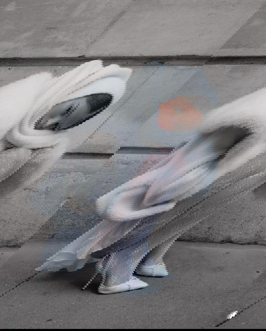 Девушка в кружевных белых колготках и белых лодочках, пушистое белое пальто и шарф, поза у стены — романтичный зимний сет для фотосессии