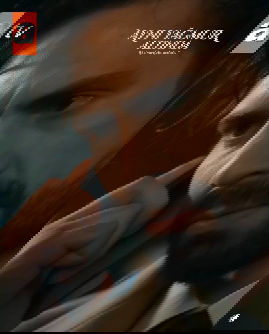 Крупный план Таро Эмир Текин с телефоном, напряжённое выражение лица — кадр промо с логотипом atv и названием сериала «Ayni Yağmur Altında».