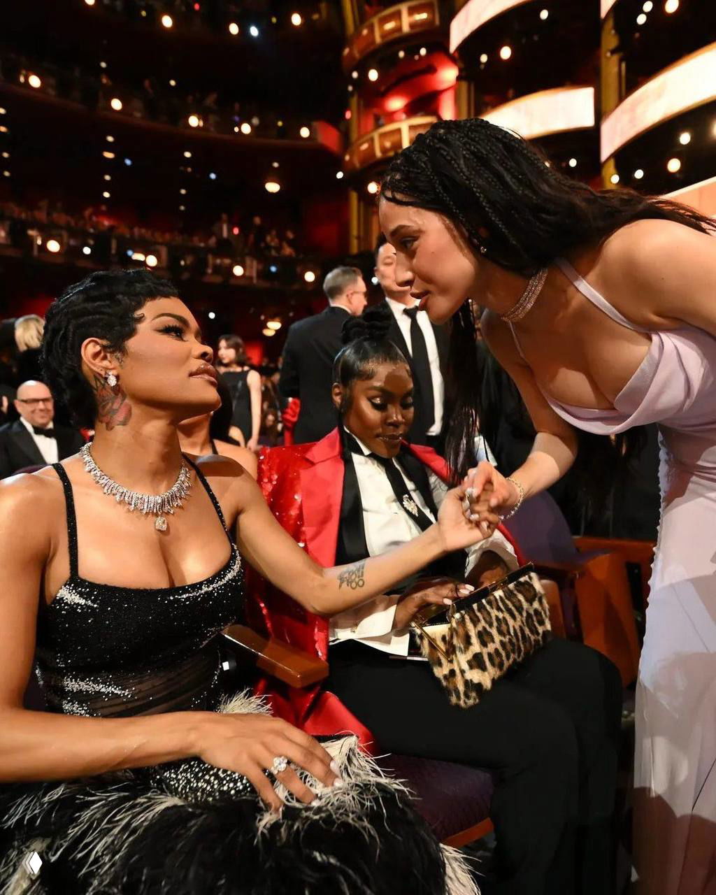 Несколько гостей в зале обмениваются рукопожатиями и словами, видны ложи театра и аудитория на фоне церемонии.