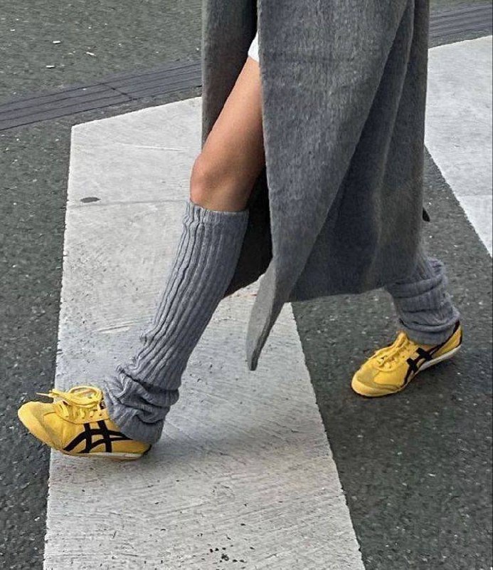 Крупный план ног в серых высоких гольфах и жёлтых кроссовках, гольфы собраны складками — спортивно-небрежный уличный стиль для прохладной погоды.