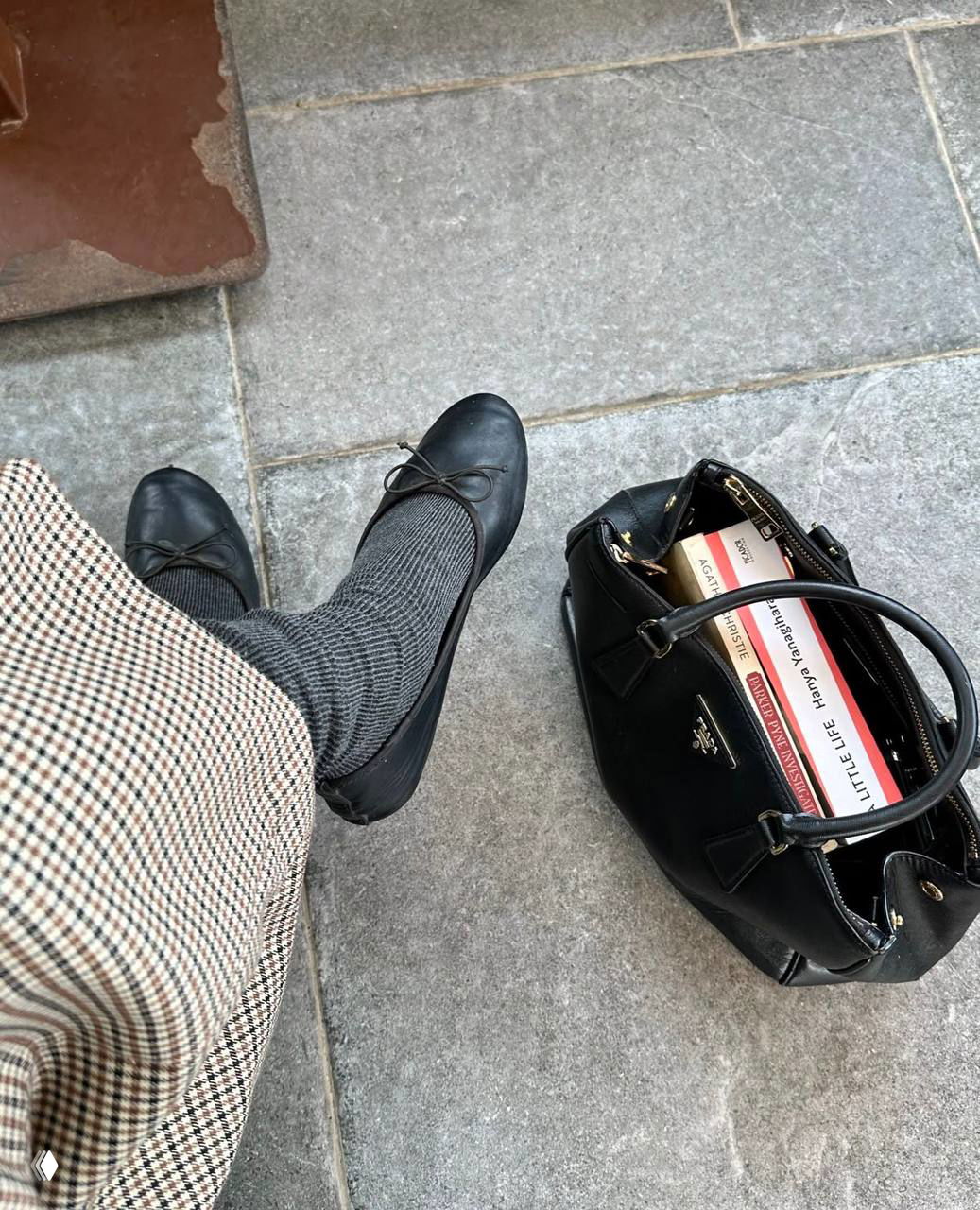 Низкий ракурс: элегантные чёрные балетки без декора, серые носки и чёрная сумка с книгами стоят на тротуаре — весенний повседневный look.