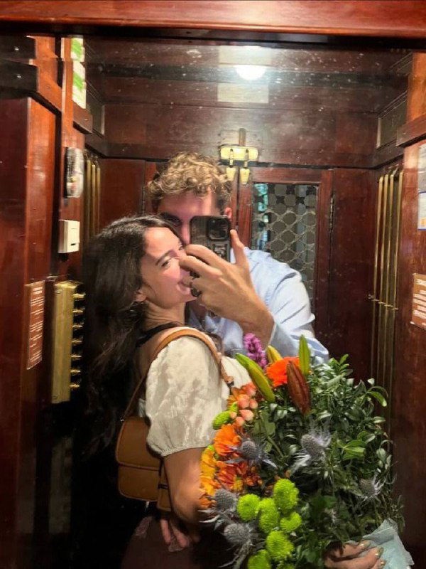 Зеркальное селфи пары в лифте: парень обнимает девушку, в кадре большой букет цветов и тёплая атмосферная обстановка.