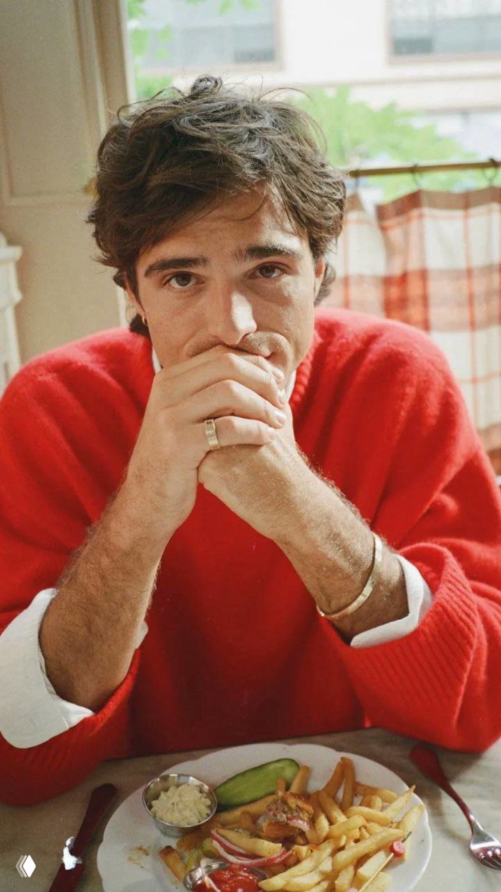 Портрет мужчины в красном свитере за столом с тарелкой и картофелем фри; кадр в уютной домашней обстановке и мягком естественном свете.