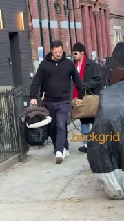 Кадр папарацци: Гарри Стайлс с большой дорожной сумкой и Зои Кравиц рядом, уличная сцена в городском окружении Нью‑Йорка.