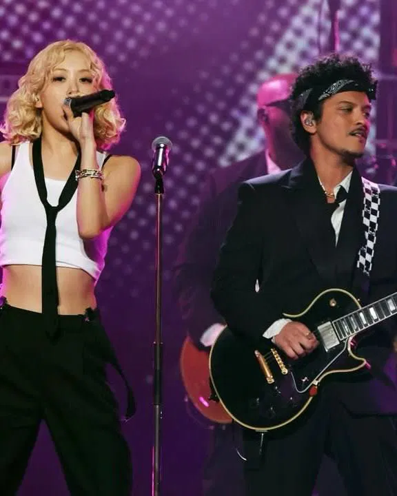 Певица и гитарист на сцене во время живого выступления; сцена подсвечена розовыми и фиолетовыми прожекторами.