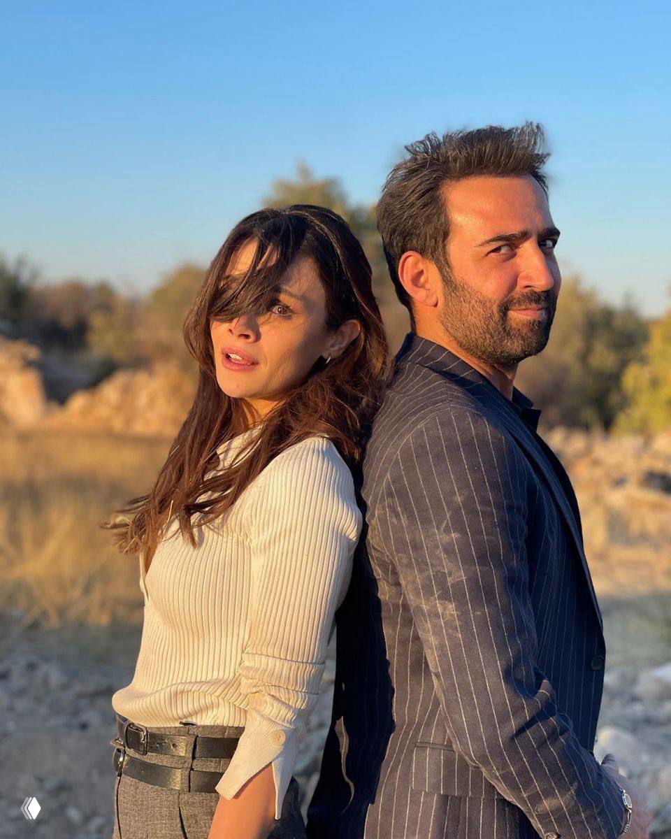 Алья и Джихан стоят спиной друг к другу на природе в лучах закатного солнца, повседневные образы и локация на открытом воздухе.