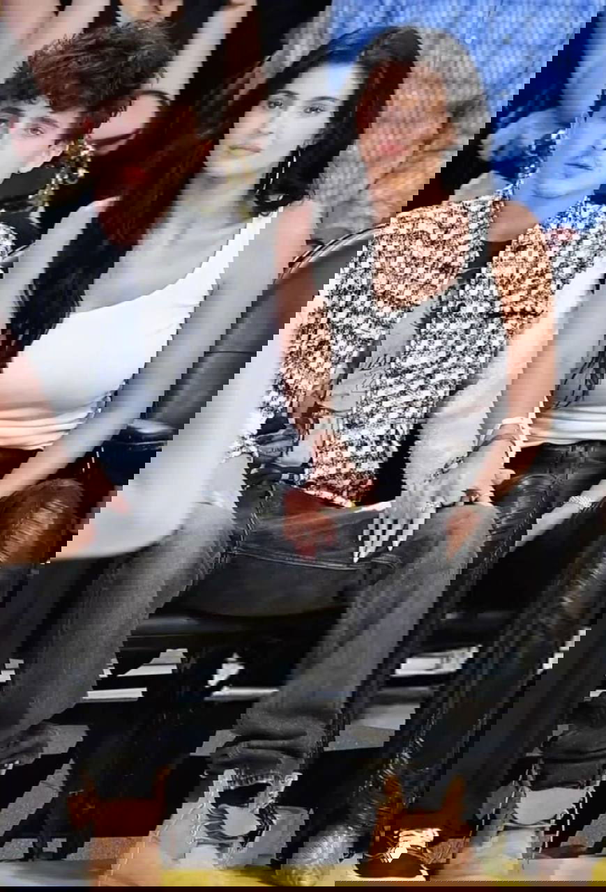 Мужчина и женщина сидят в первом ряду, держатся за руки; повседневная одежда и окружающая толпа указывают на спортивное или развлекательное событие.