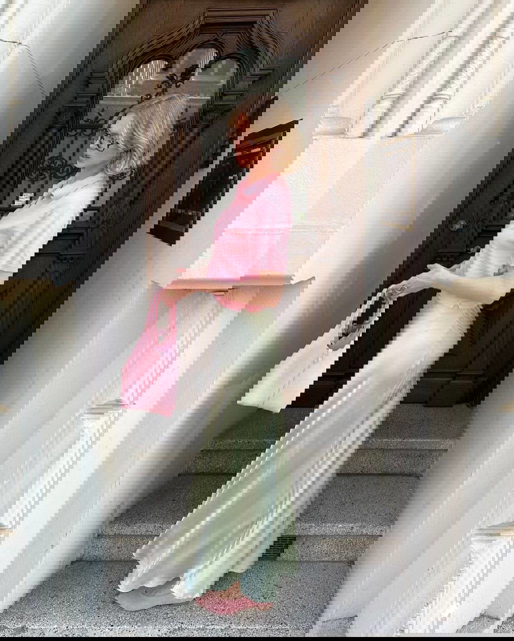 Полный образ: женщина в светло-мятной атласной юбке и розовой футболке, пастельное сочетание тонов на ступеньках у входа в здание.