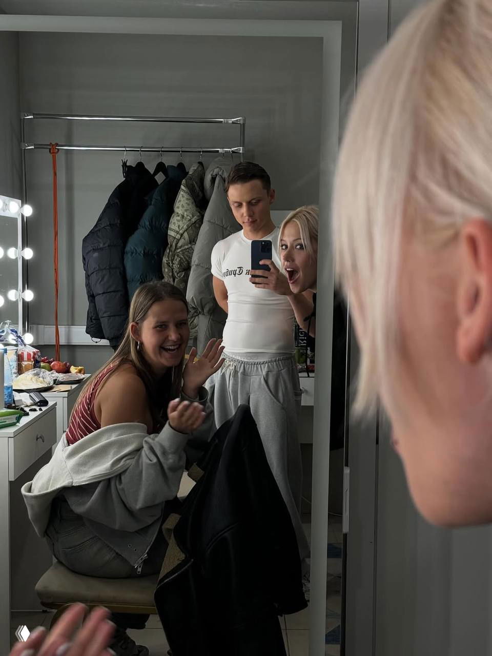 Зеркальное селфи из гримёрки: Ваня делает снимок на телефон, рядом смеются друзья и коллеги, непринуждённая подготовка к выступлению.