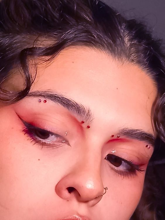 Портретный снимок с лёгким красным макияжем и мелкими стразами у внешнего уголка глаза на смуглой коже.