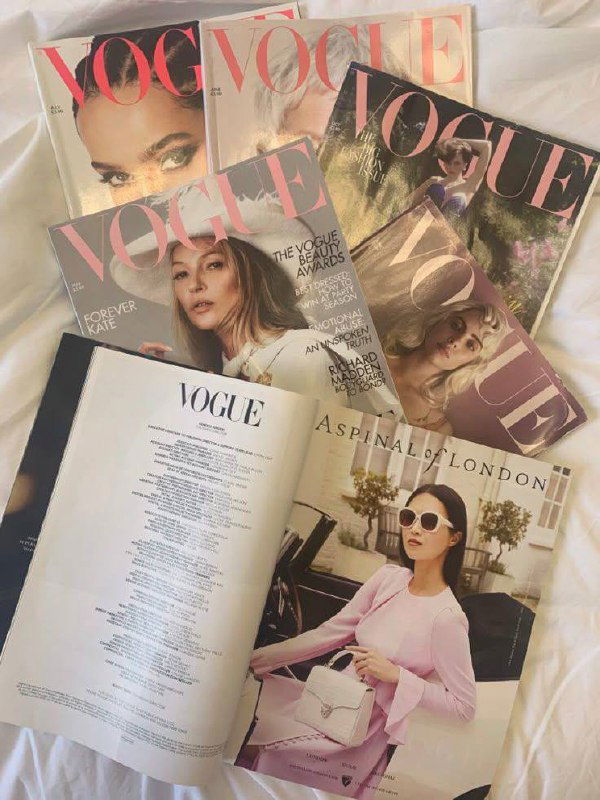 Несколько экземпляров журнала Vogue и раскрытая страница с рекламой, разложенные на постели — стопка модных изданий и журнальная композиция.