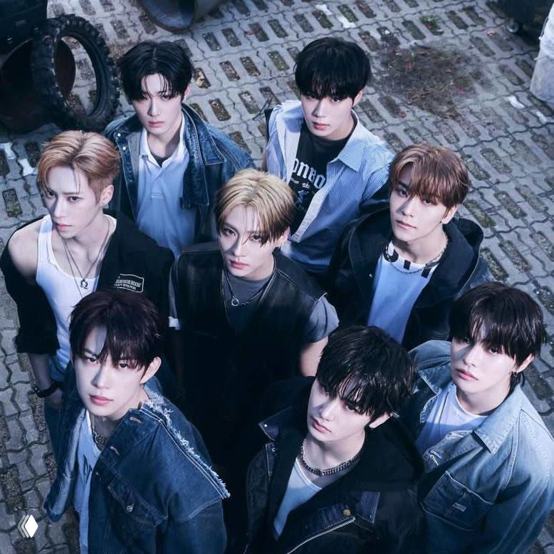 Групповое промо‑фото k‑pop коллектива: несколько молодых артистов в модных образах на урбанистическом фоне, студийная стилизация.