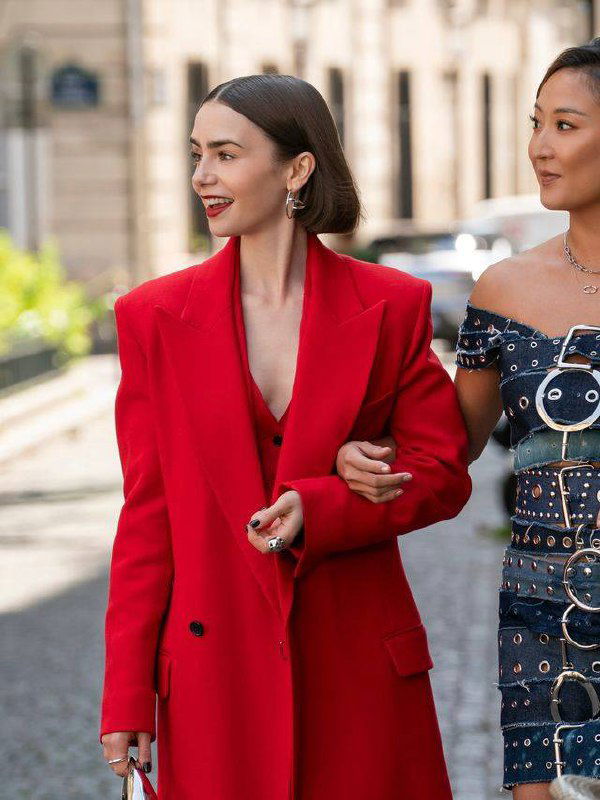 Героиня в ярком красном оверсайз-пиджаке идет по городу, рядом подруга в декорированном платье; солнечная городская улица.