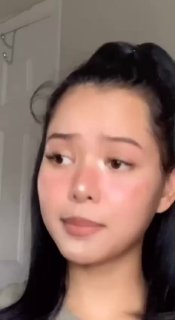 Крупный план молодой женщины с нейтральной мимикой в вертикальном формате — кадр из короткого TikTok липсинг‑видео, бытовой фон за спиной.