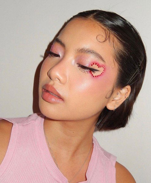 Модель с сияющей кожей и декоративными стразами вокруг глаза, макияж в розово-красной гамме для праздника.