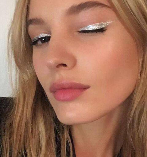 Полупрофиль модели с тонкой серебряной стрелкой на веке и мягким нюдовым макияжем губ — аккуратный праздничный образ.