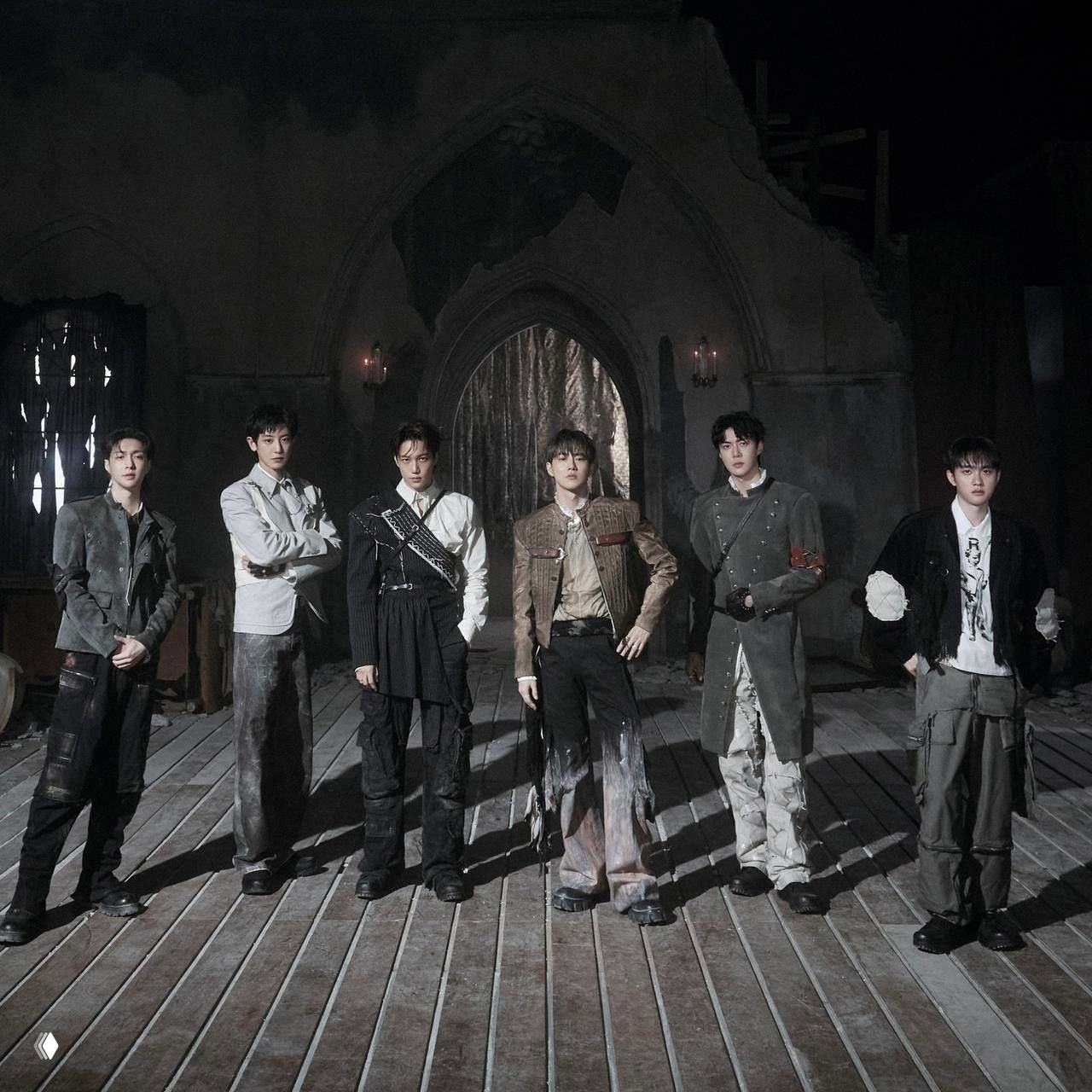 Промо‑кадр в готической студийной декорации: несколько артистов в стилизованных костюмах на тёмном фоне с архитектурными элементами.