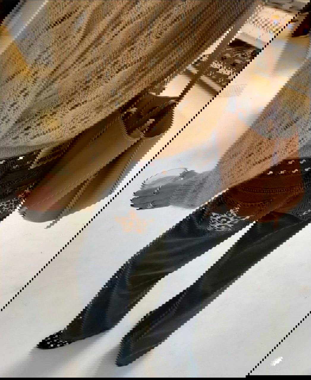 Девушка в тёмных джинсах с леопардовой звездой на задних карманах, вязаный свитер и большая сумка; акцент на декоре карманов и образе.