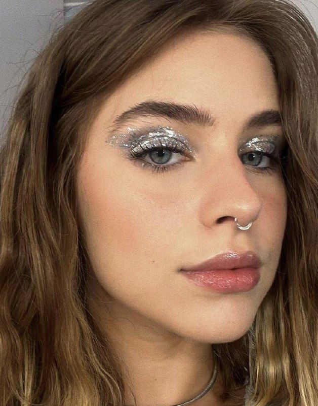 Молодая женщина с плотным серебристым глиттером на подвижном веке, естественными бровями и нюдовыми губами для фешн-образа.