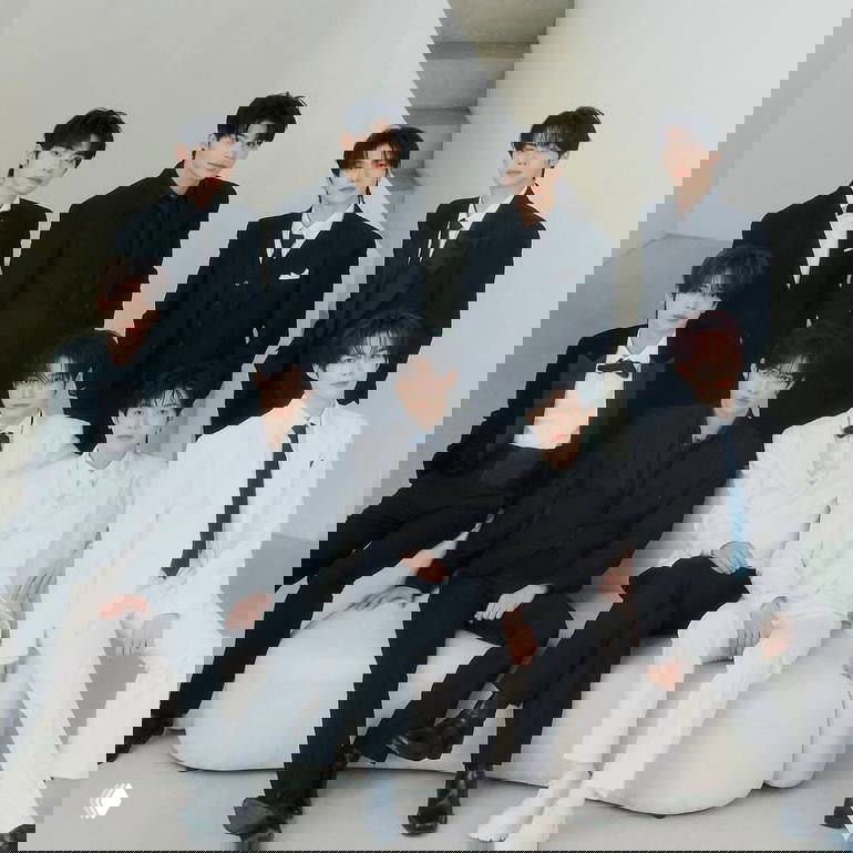 Формальное групповое фото k‑pop коллектива: участники в смокингах и классических костюмах на светлом минималистичном фоне.