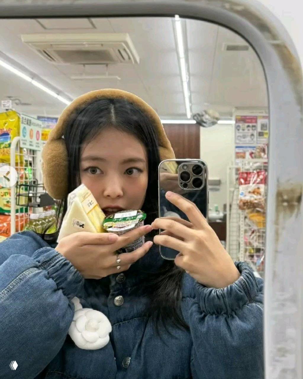 Девушка делает селфи в зеркале в магазине, держит несколько упаковок перекуса и смартфон, вокруг видны яркие витрины и ценники