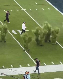 Исполнитель идёт по полю рядом с несколькими фигурами в костюмах «живой травы» во время шоу Бэд Банни на Супербоула 2026.