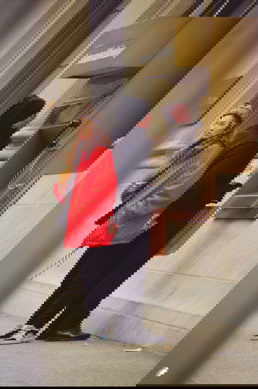 Кадр: женщина в чёрном пальто и мужчина в жилете и повязке идут по улице — минималистичные и лаконичные образы героев сериала