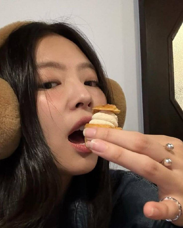 Крупный план молодой женщины с наушниками, она приближает к рту небольшой десерт и готовится укусить, фокус на еде и губах