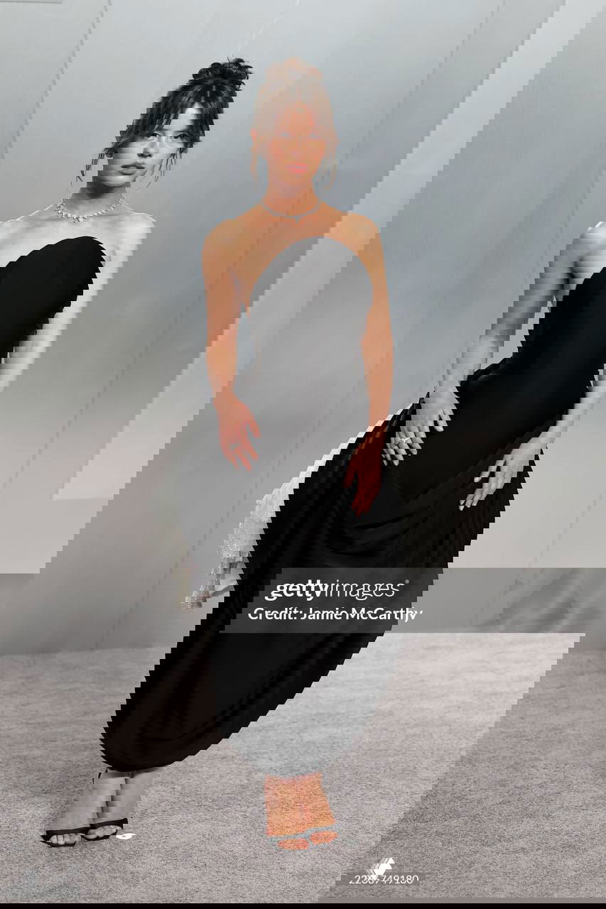 Модель в чёрном платье со сложным драпированием и открытым лифом, минимальные украшения и аккуратная причёска на афтепати.