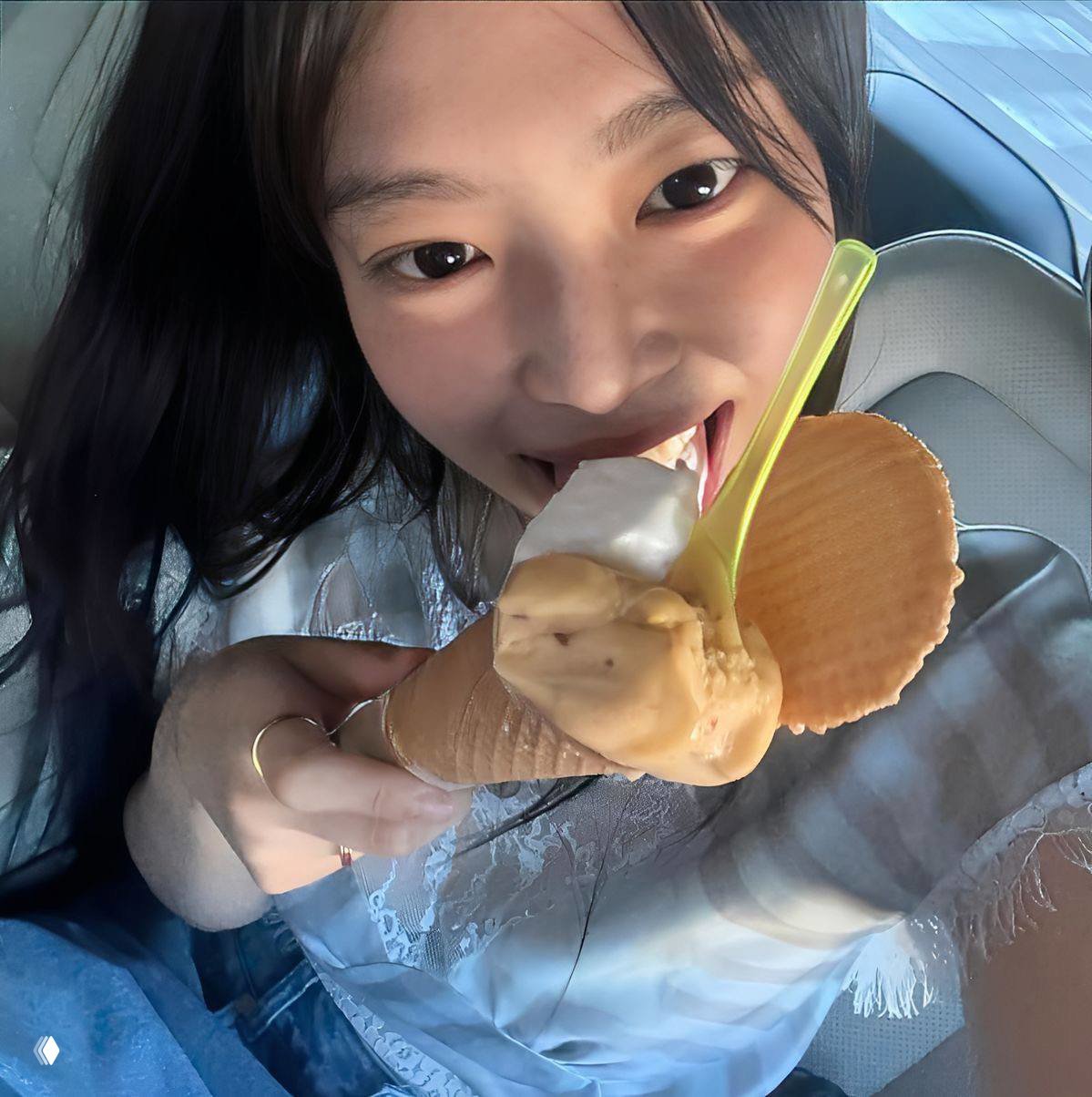 Крупный план девушки с мороженым в рожке и ложкой, она улыбается и пробует десерт в автомобиле или другом закрытом пространстве