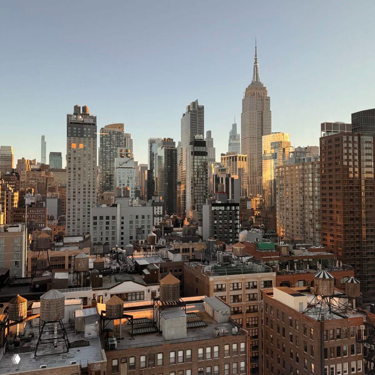 Городской панорамный вид с высотными зданиями и небоскрёбом на горизонте, тёплое вечернее освещение и крыши большого города.