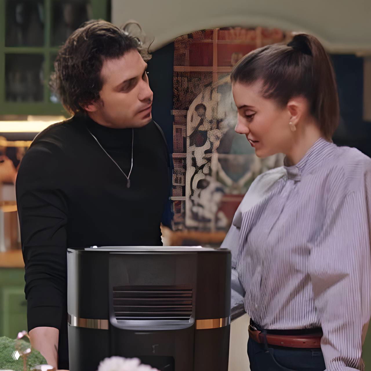 Персонажи сериала обсуждают что-то у бытовой техники на фоне кухонного интерьера; видны задумчивые и тёплые эмоции между героями.