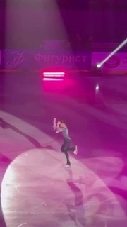 Вертикальный кадр: фигуристы на льду, один в прыжке, видны тени и фиолетовое освещение сцены во время шоу teamTutberidze