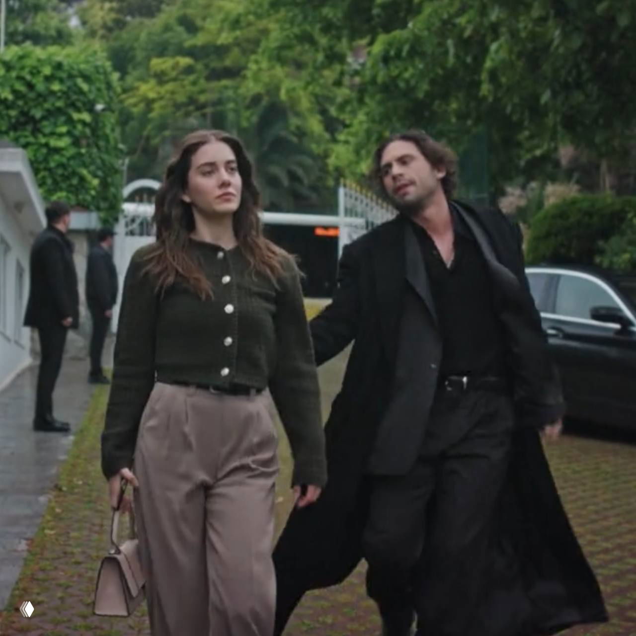 Герои выходят на прогулку у ворот фешенебельного дома; мужчина делает попытку догнать или разговорить женщину, видно движение и сюжетную интригу.