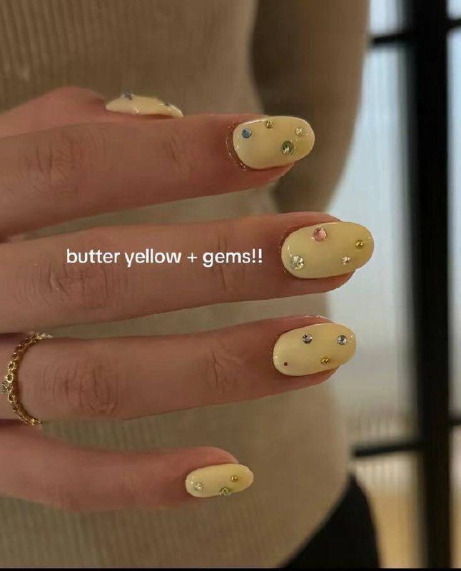 Крупный план рук с лимонно‑жёлтым покрытием и декоративными кристаллами: мягкий butter yellow и несколько разноцветных стразов для сияния.