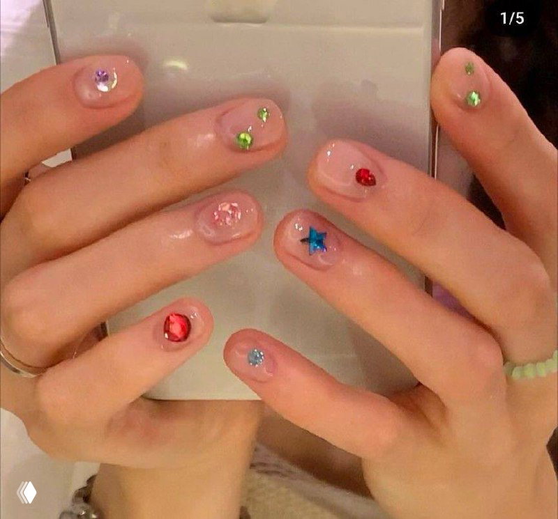 Рука в фокусе с прозрачным глянцевым покрытием и мелкими разноцветными стразами: минималистичный, но сверкающий маникюр в деталях.