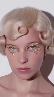 Крупный план модели с праздничным макияжем: стразы и жемчужинки по контуру глаз, светлая ретро‑укладка и мягкая тень для глянцевого эффекта.