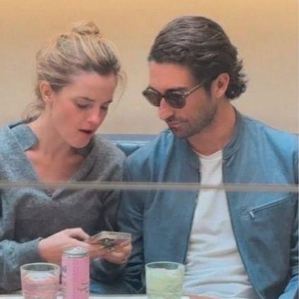 Эмма Стоун и Гонсало Эвия Байерес за столиком в ресторане: актриса показывает что-то на телефоне, мужчина в солнцезащитных очках внимательно смотрит.