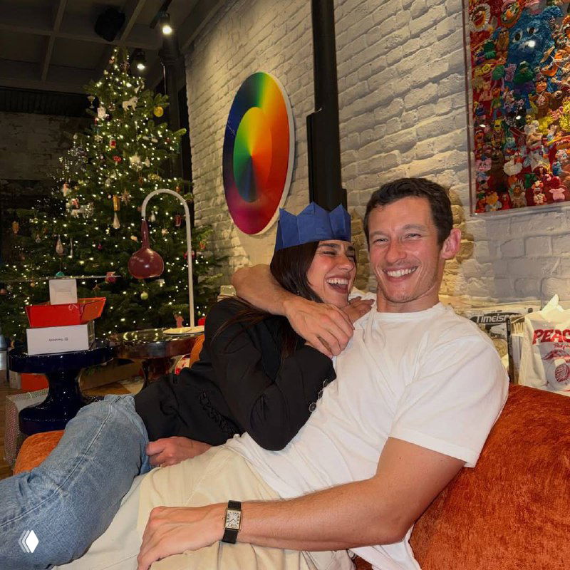 Двое людей смеются на фоне рождественских огней и кирпичной стены; снимок заметно искажен цифровыми артефактами