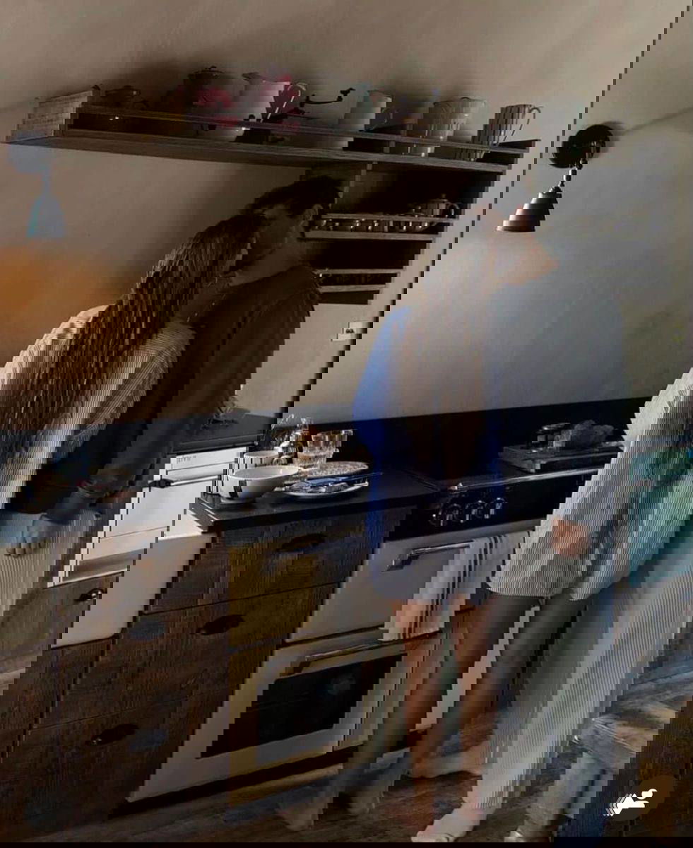 Пара целуется на кухне в уютной атмосфере: женщина в длинной рубашке, мужчина в домашней одежде, стилизованный интерьер.