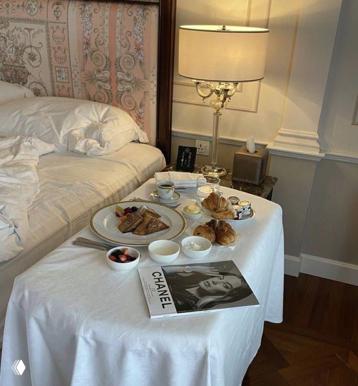 Поднос с завтраком и журналом Chanel на столике у постели — уютная интерьерная сцена с пастельной эстетикой и элементами роскоши.