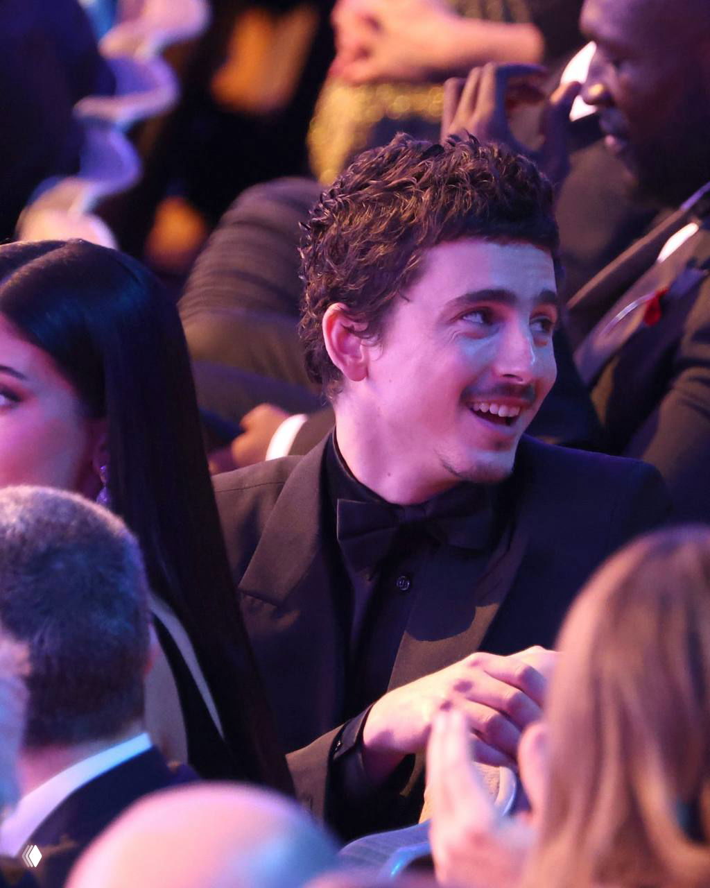 Крупный план мужчины в смокинге, снятый на церемонии BAFTA: живое выражение лица и атмосфера мероприятия вокруг.