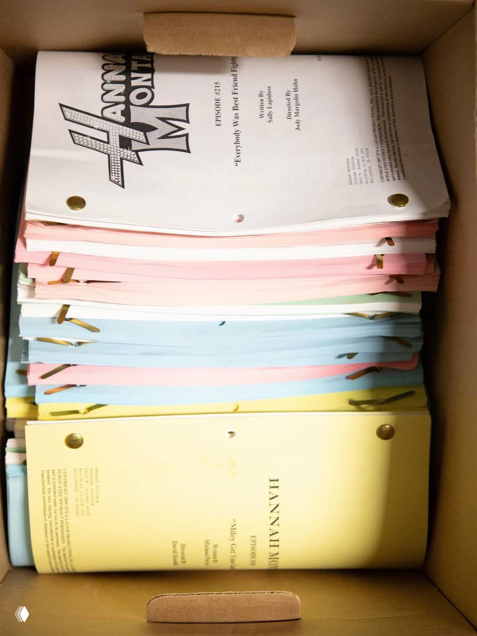 Коробка со стопкой сценариев и брошюр пастельных цветов — архивные страницы сериала «Hannah Montana» в пачке.