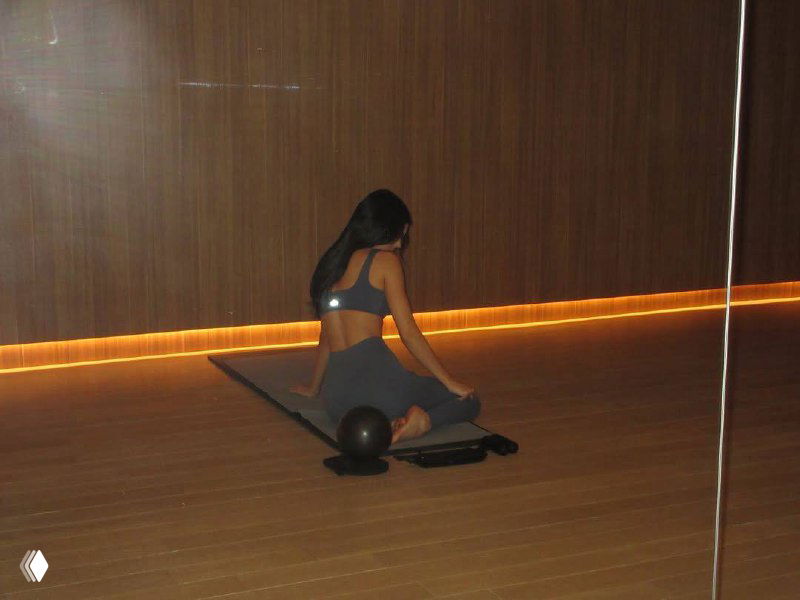 Искажённый кадр тренировки в студийной обстановке: силуэт участницы в позе на полу у зеркальной стены, линии света и пикселизация по кадру.