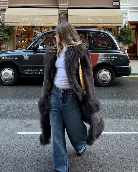 Уличный кадр: женщина в тёмно-синем афганском пальто с пушистым ворсом, свободные джинсы и городской осенний фон с припаркованными автомобилями