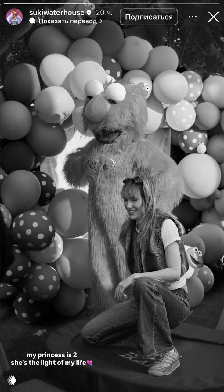 Чёрно‑белое фото с праздника: женщина на корточках рядом с персонажем в костюме и аркой из шариков, снимок из сторис с подписью о двухлетии.