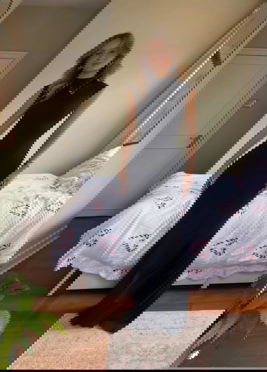 Малин в элегантном чёрном вечернем платье в полный рост на фоне спальни — классический вариант для формальной новогодней вечеринки.